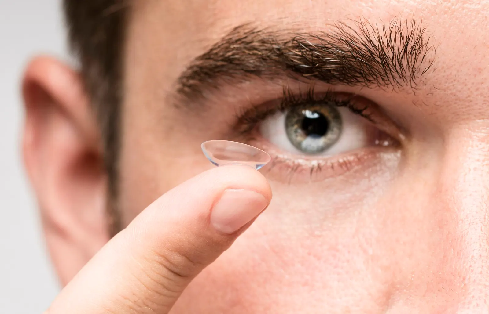 Mann hält eine Kontaktlinse vor sein Auge
