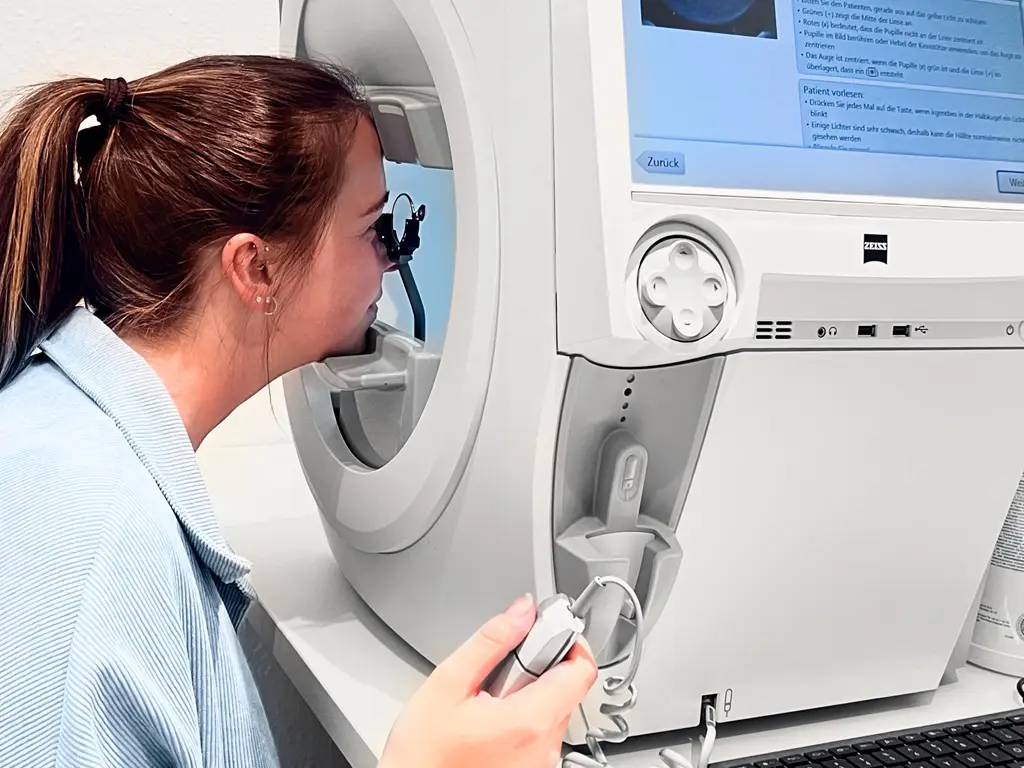 Patientin schaut durch eine Linse am kinetischen Perimeter